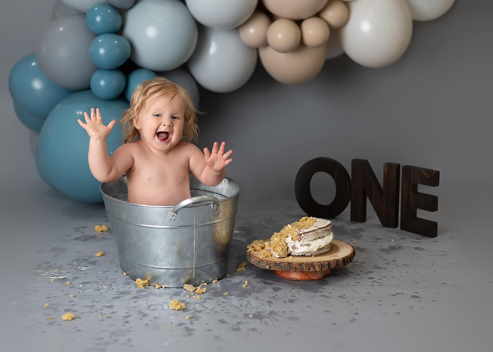 a baby boy on his first birthday with a balloon arch and cake