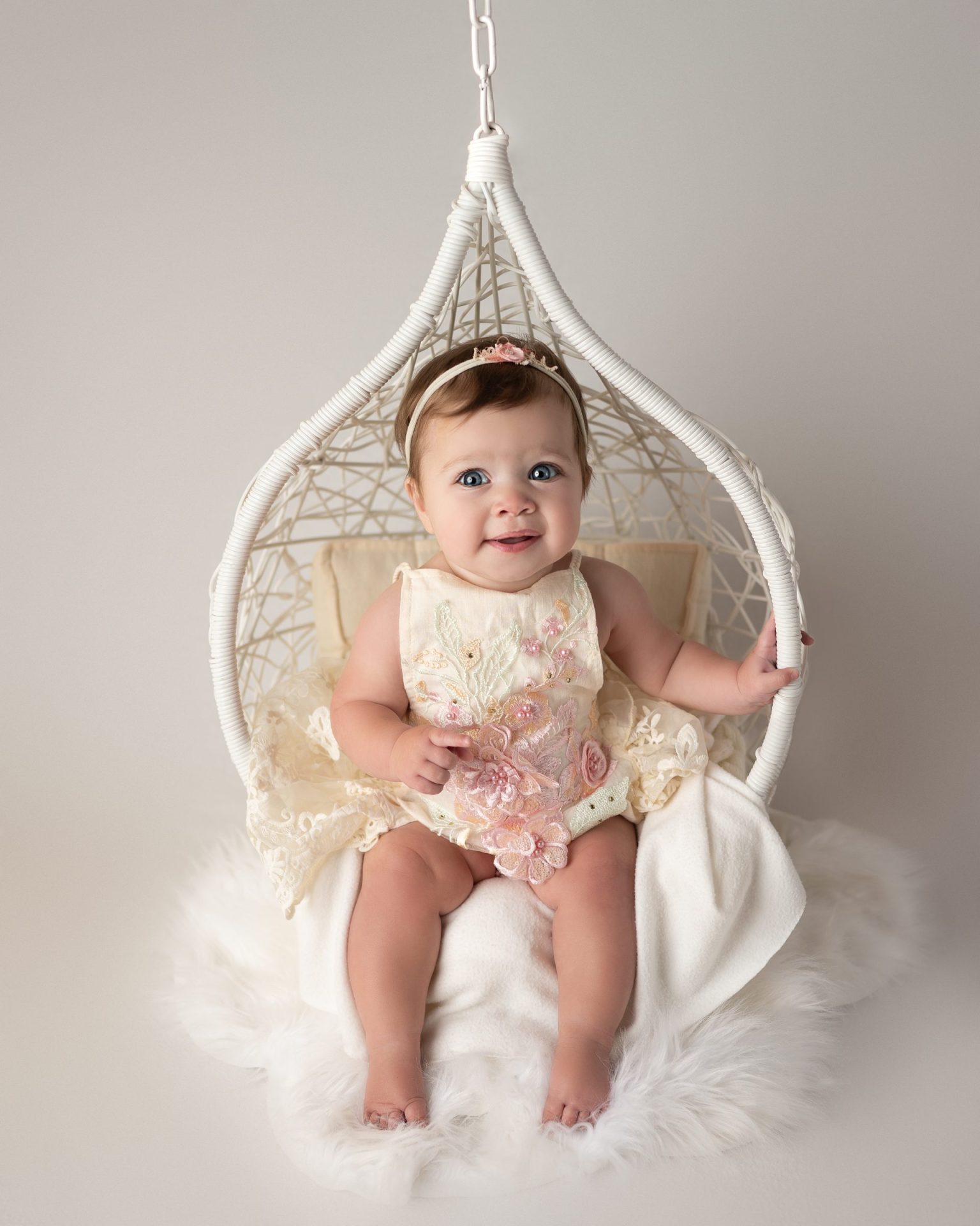 a 6 month baby girl posed in a prop swing with neutral colors