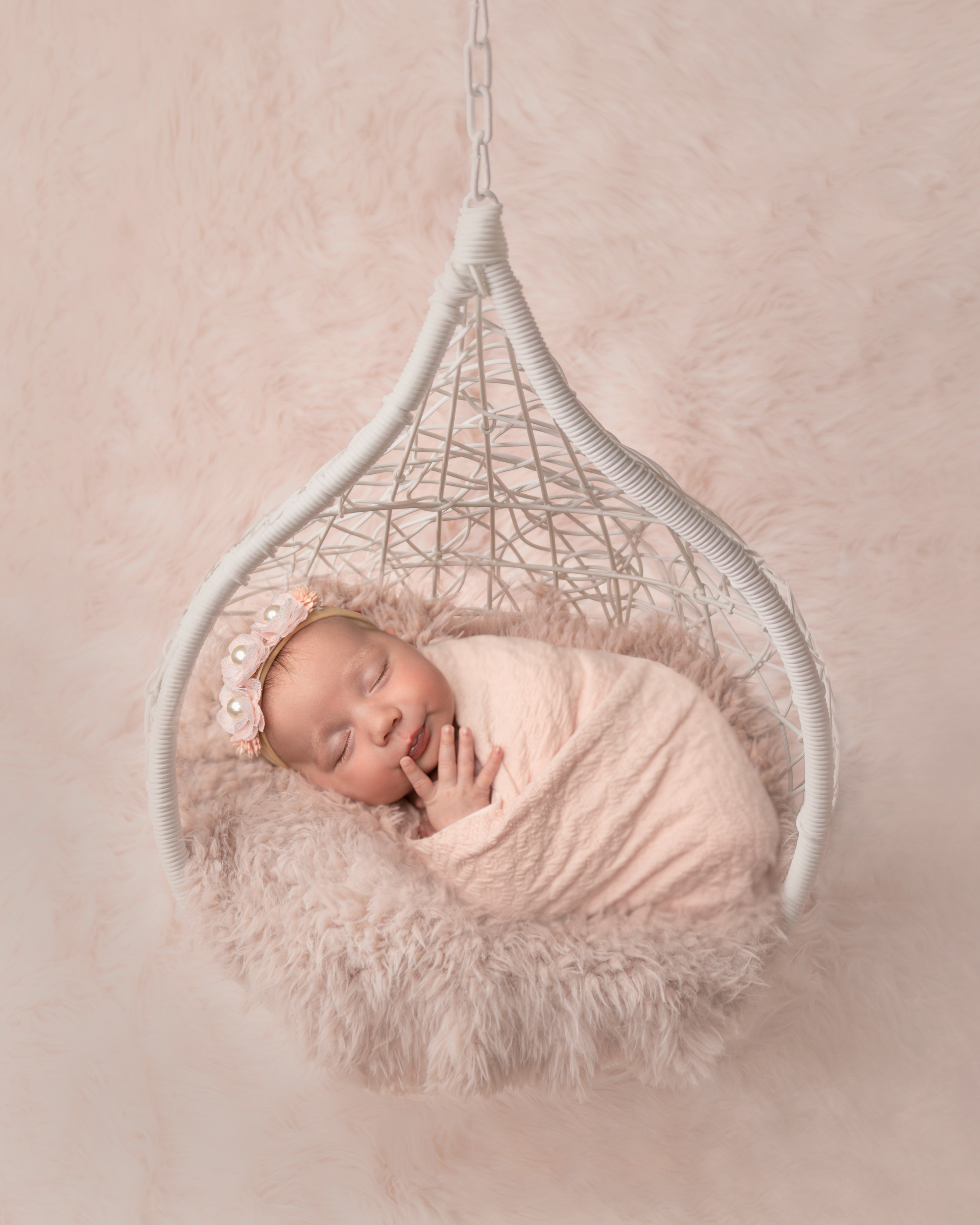 Baby girl posed on a swing swaddled in a soft peach textured layer by Sarasota newborn Photographer Lisa Bigness