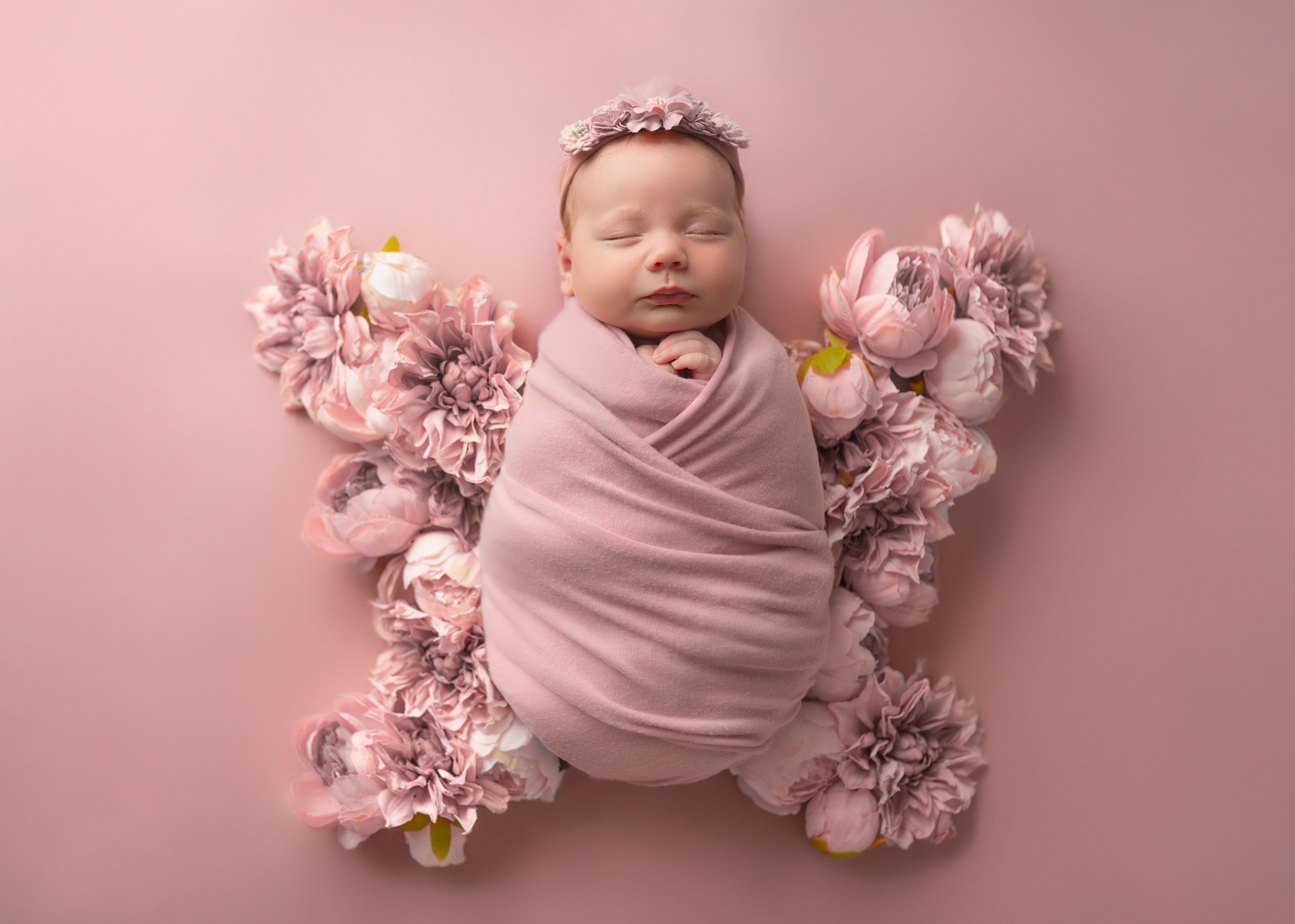 a newborn baby girl swaddled and placed in a bed of flowers arranged like butterfly wings