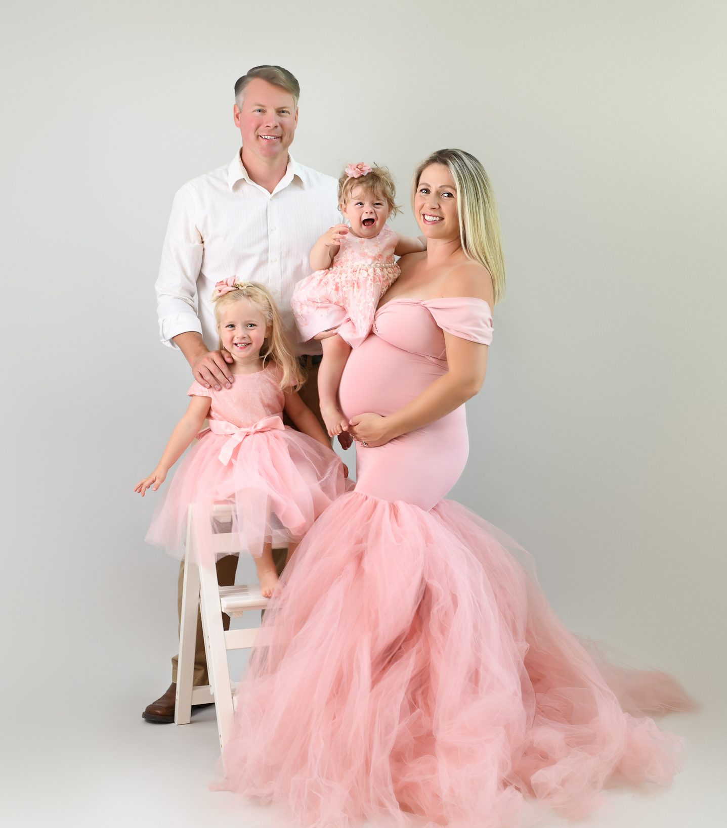 a pregnant mother posed with her 2 daughters and husband in a classic family photo