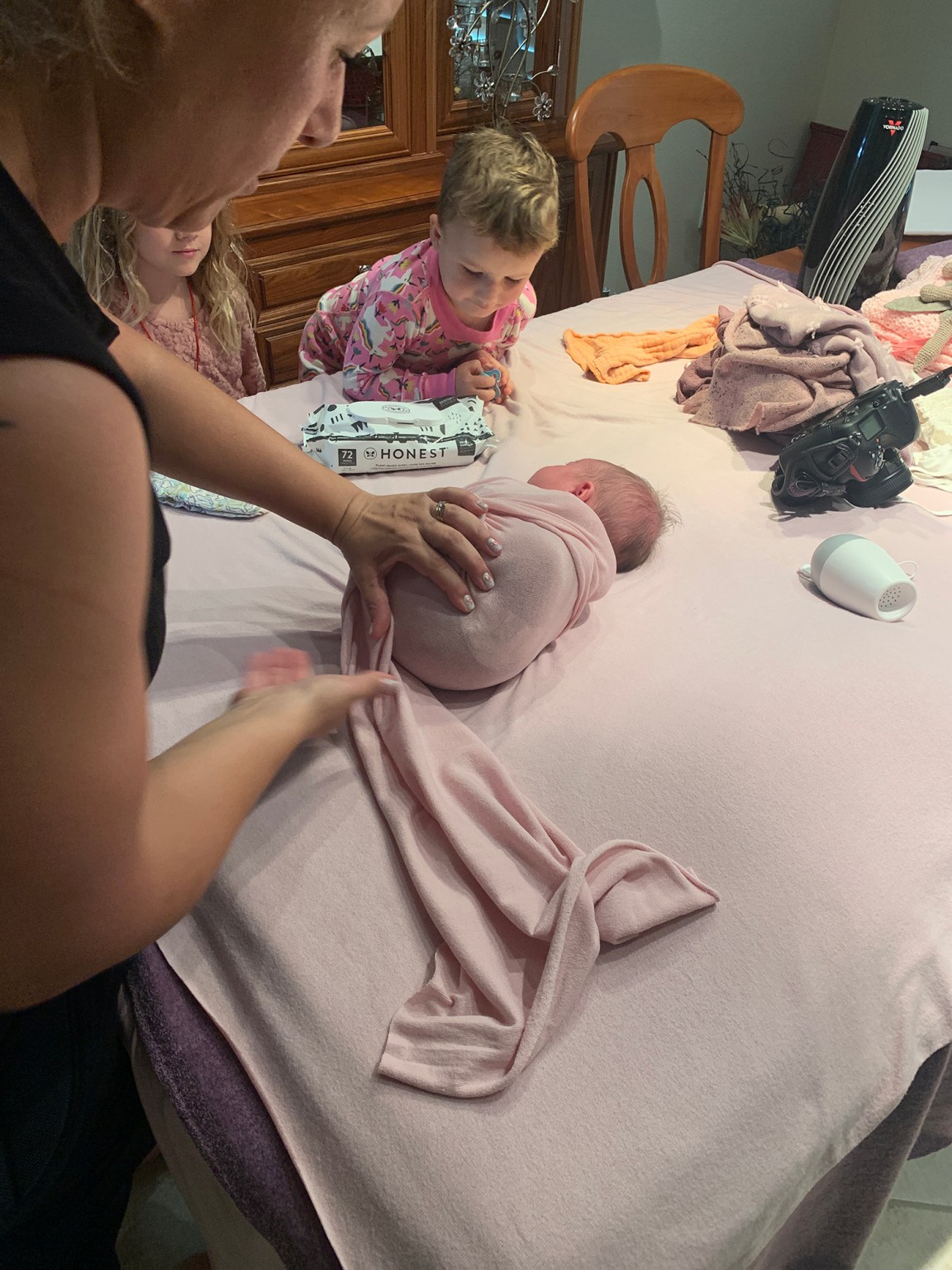 Professional Sarasota newborn photographer Lisa Bigness swaddling a newborn during a session while her older siblings look on - Cost of Newborn Photography in Sarasota